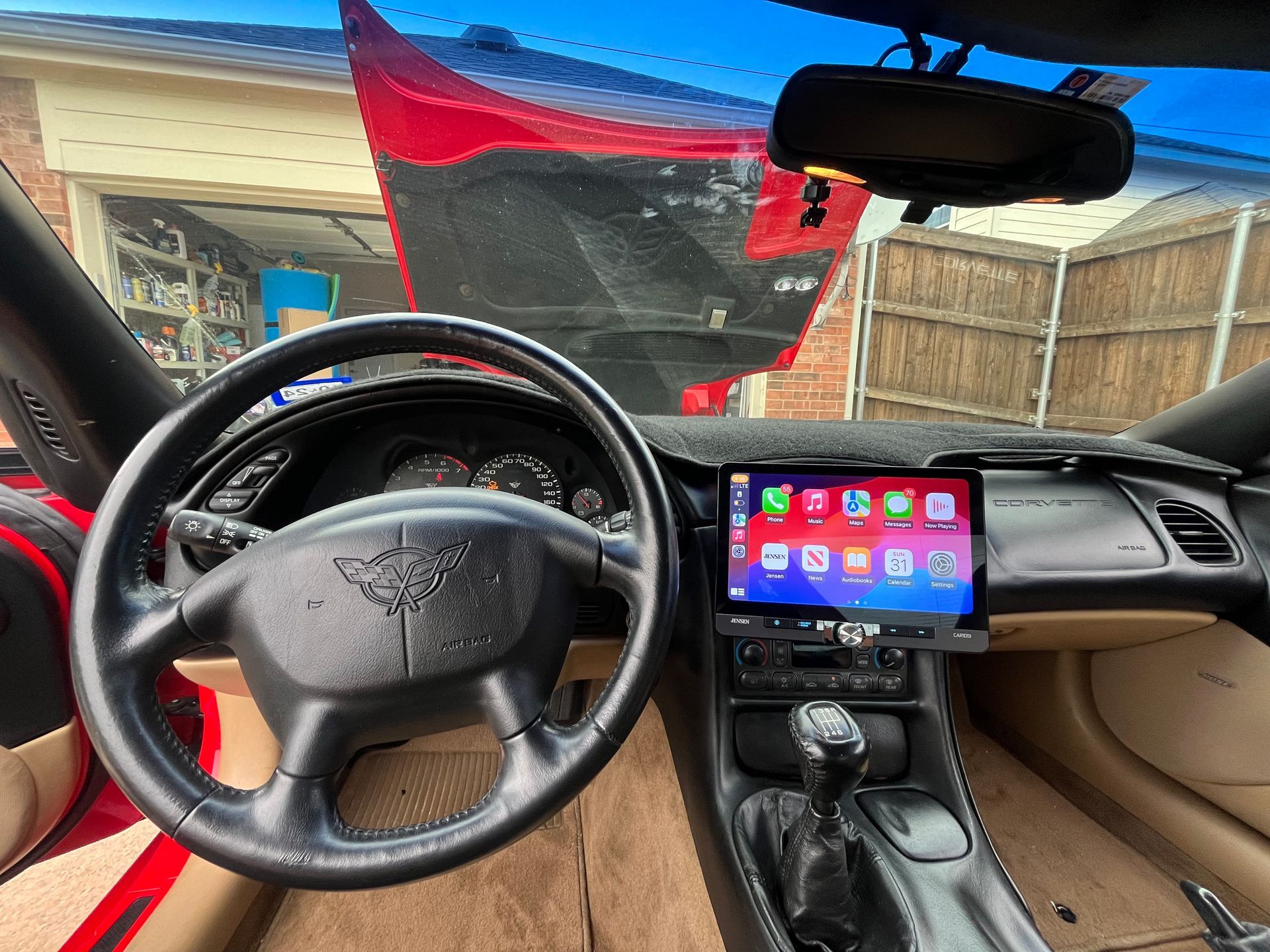 Interior of a car with steering wheel and touchscreen, tan seats, and a red windshield sunshade.