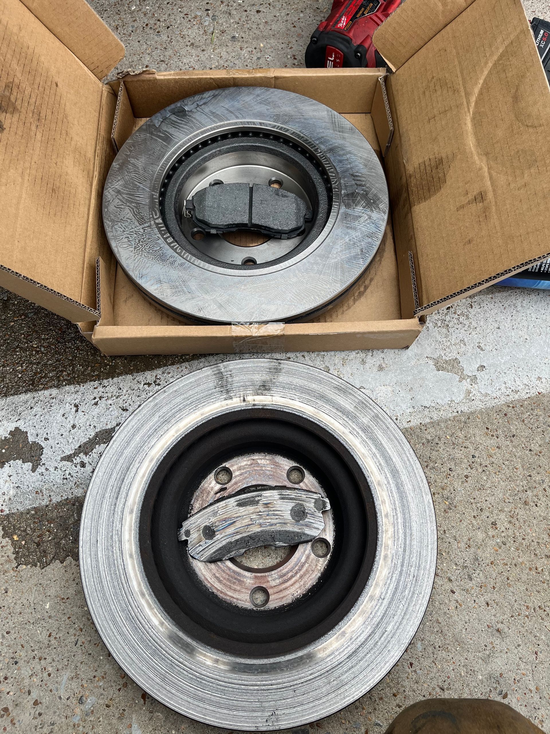 Two tire/wheel assemblies, one in a cardboard box and one on wet pavement, both dusted with frost.