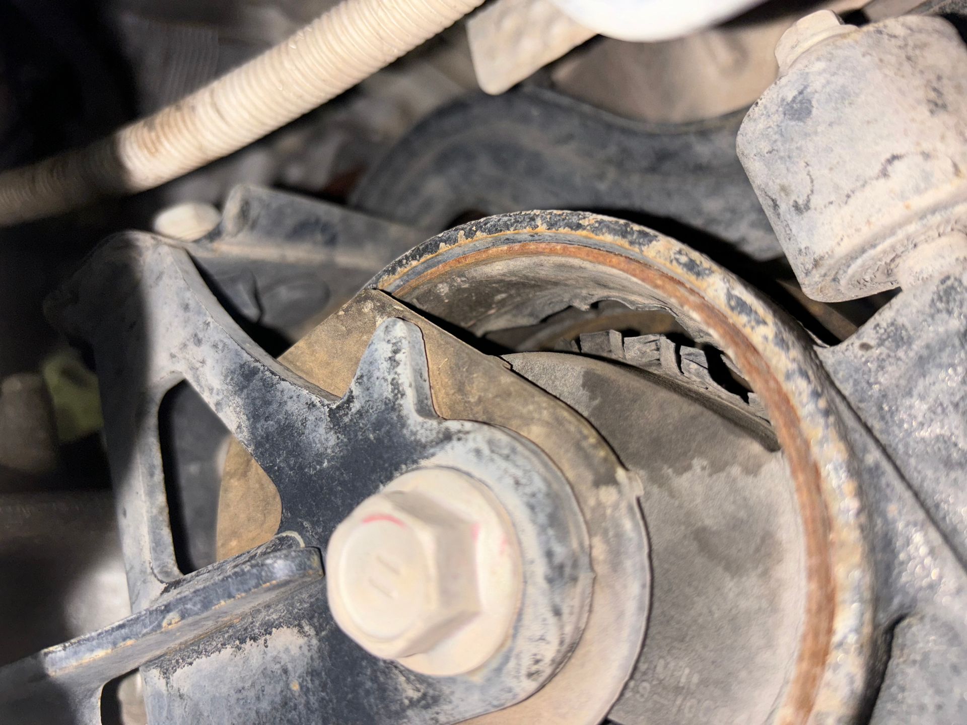 Close-up of a rusty engine pulley with a belt and central bolt in a dusty mechanical compartment