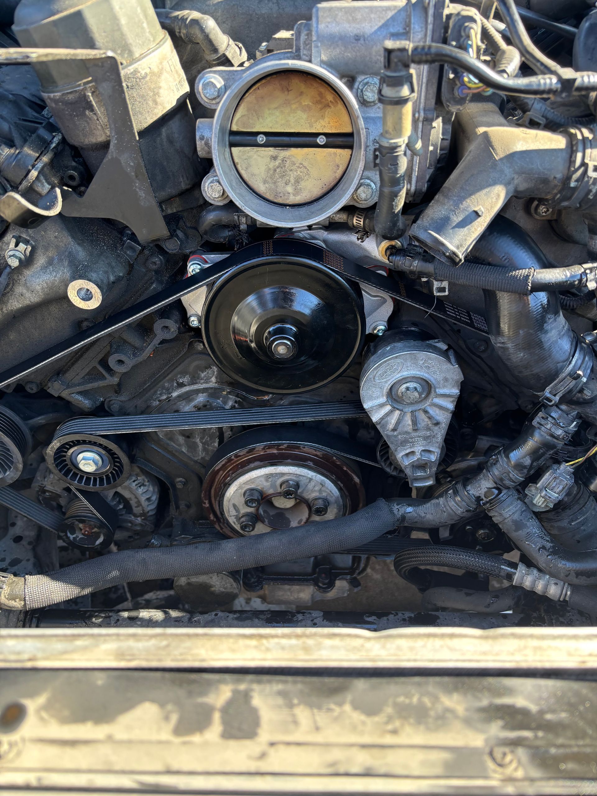 Dirty car engine with exposed timing belt, pulleys, and components under the hood