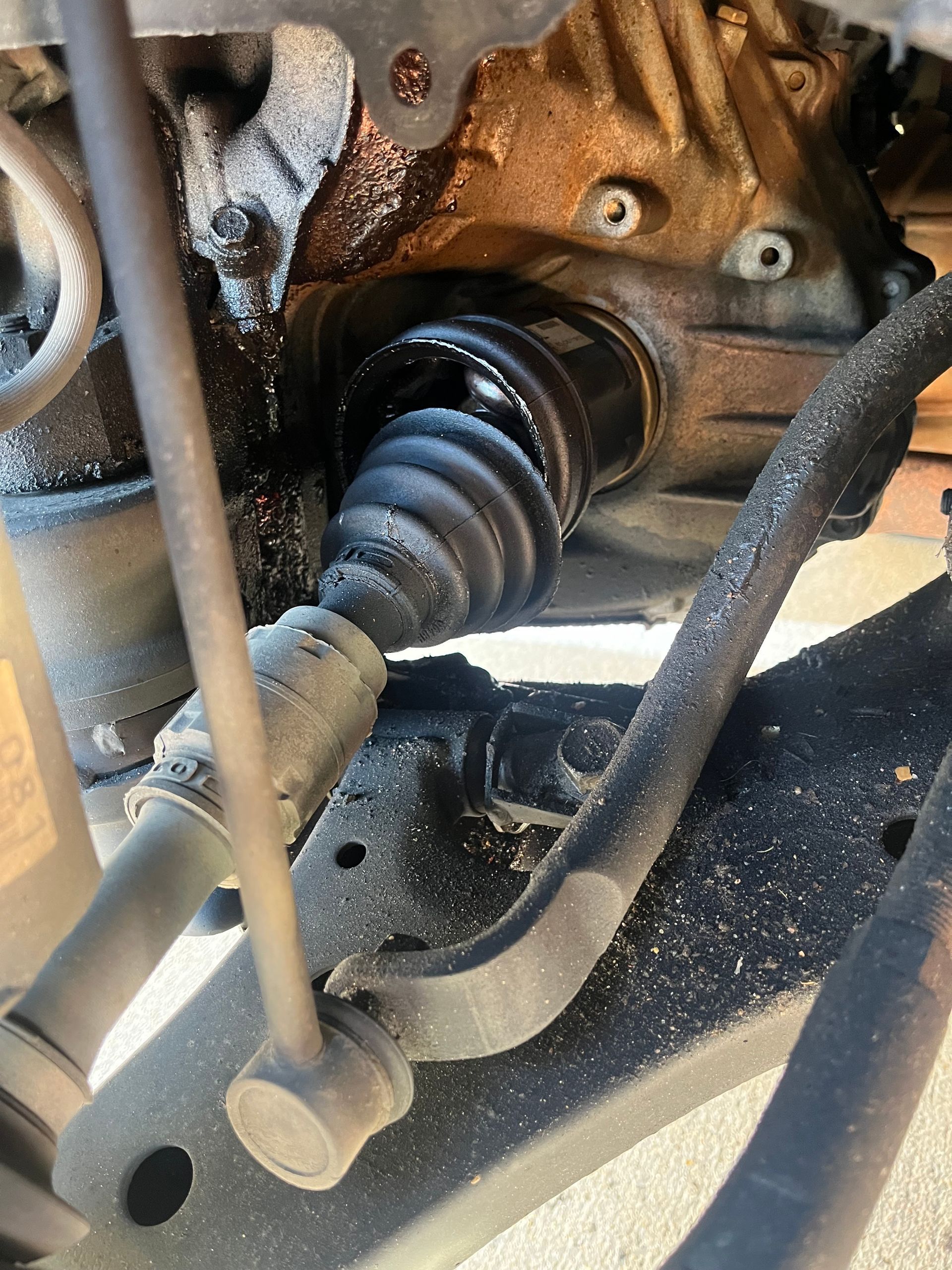 Close-up of a car’s CV axle and suspension components inside a wheel well.