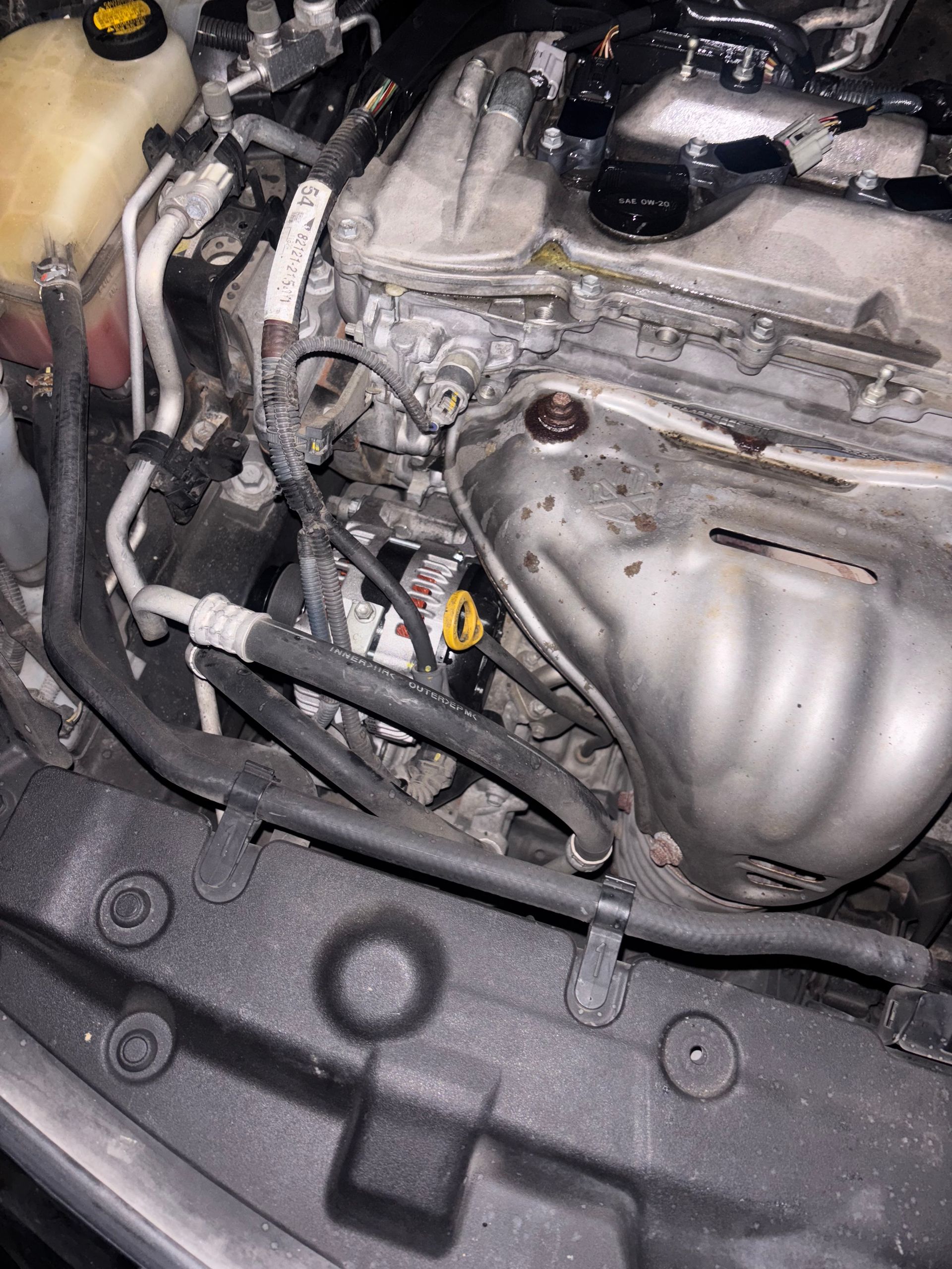 Car engine bay with silver engine cover and visible hoses in close-up.