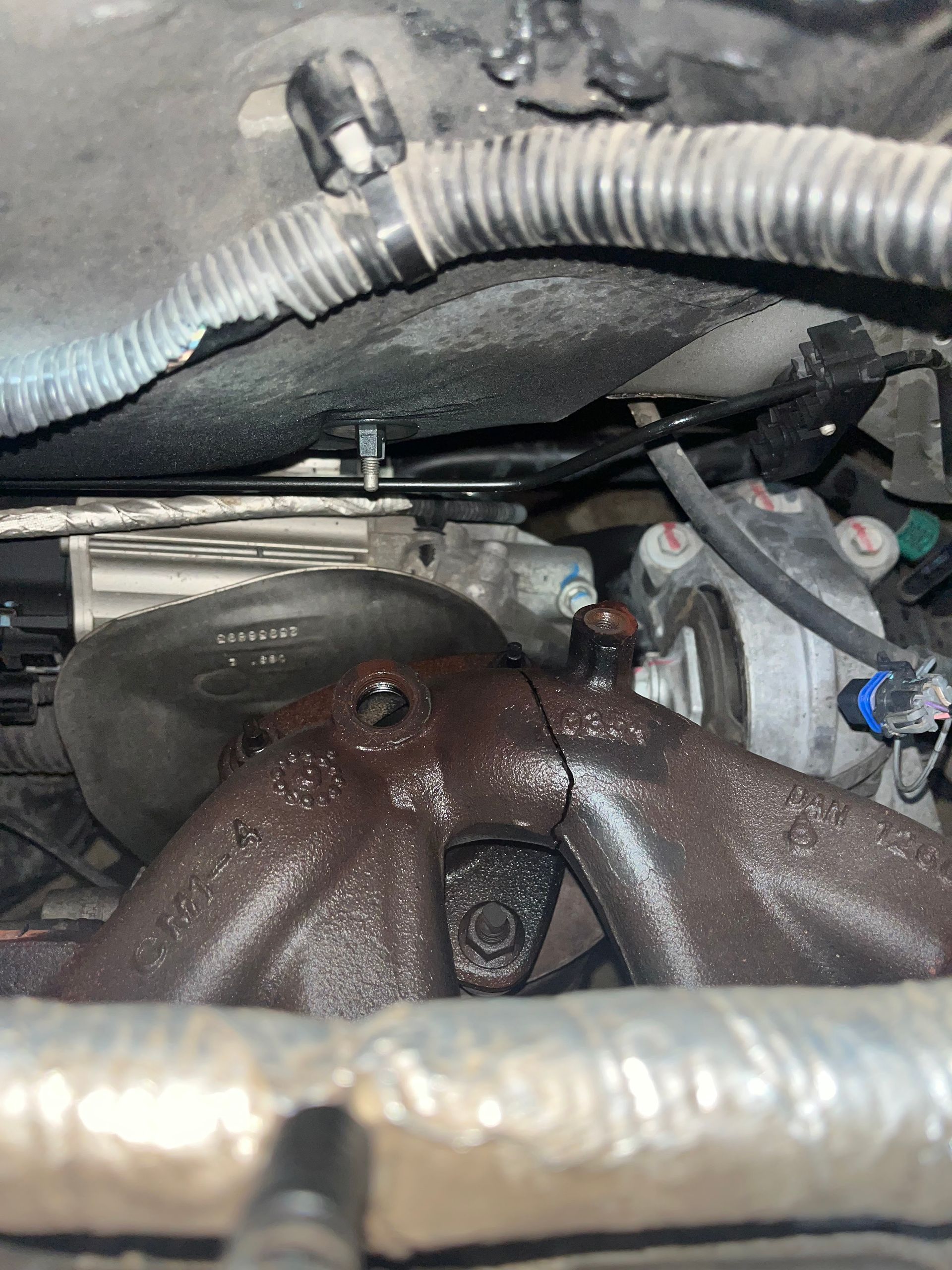 Close-up of a car engine bay with a rusted exhaust manifold and hoses visible