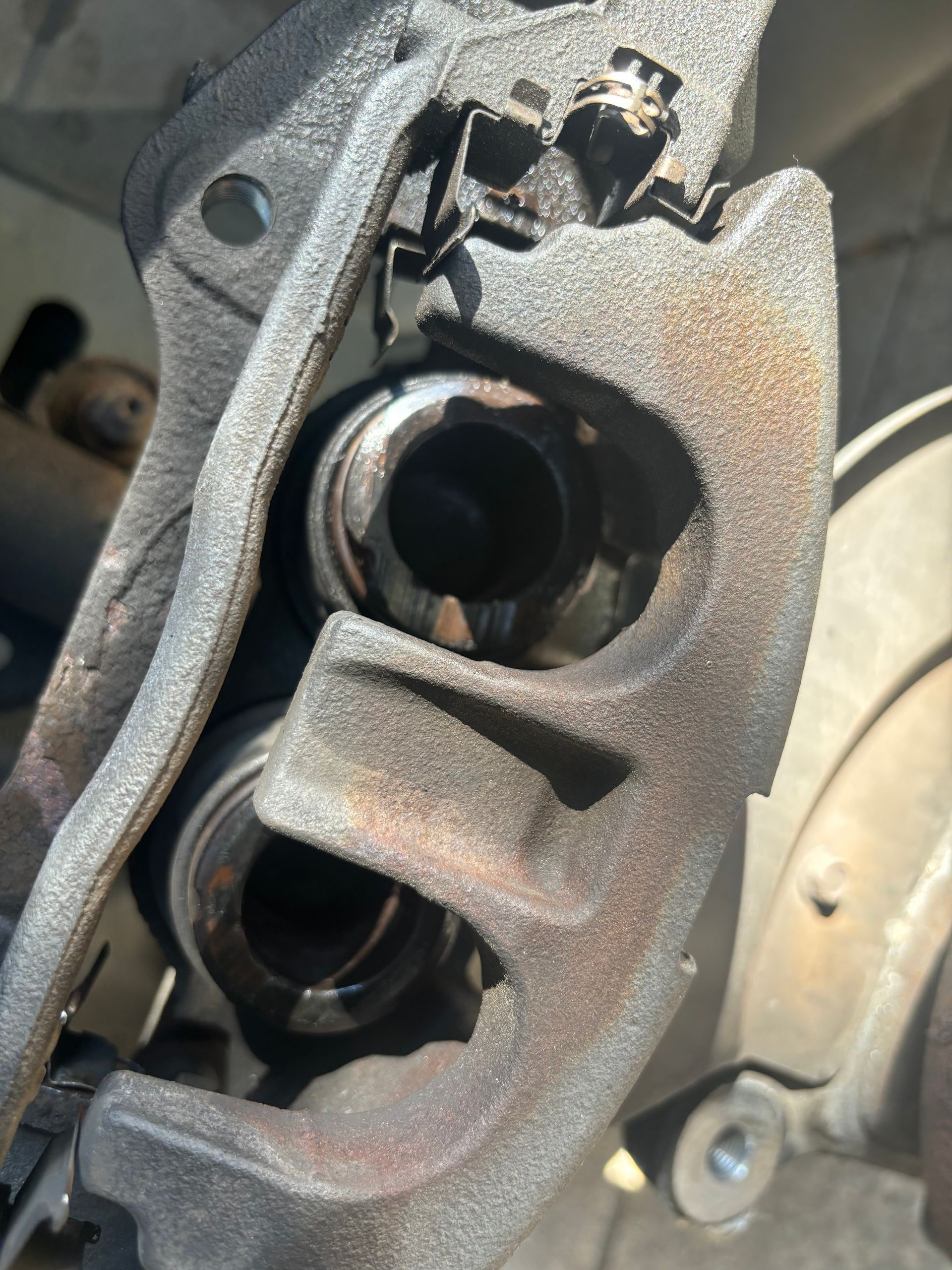 Close-up of a rusty car brake caliper with exposed piston openings and metal bracket.