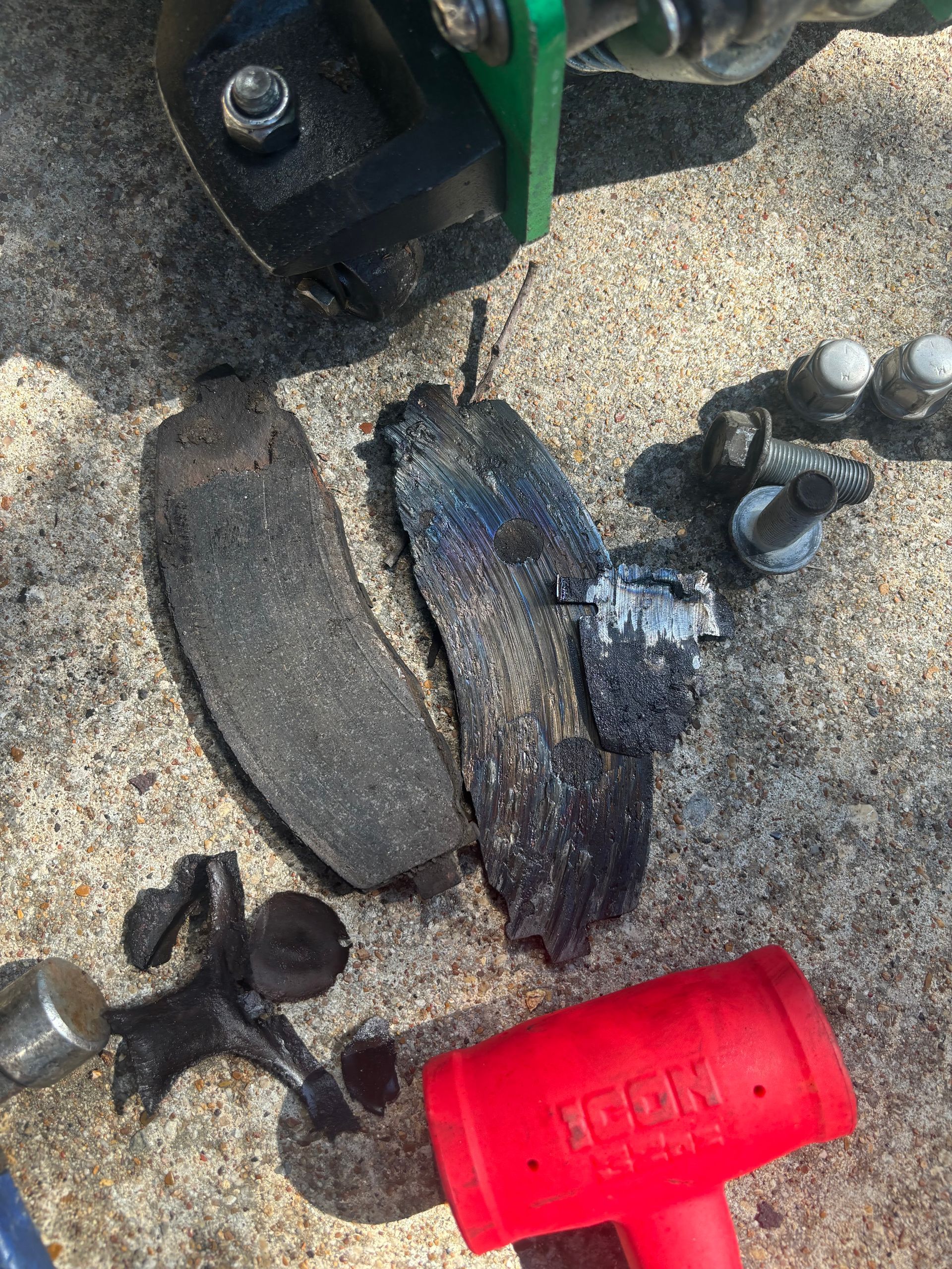 Worn brake pads and broken black car parts on pavement beside a red tool