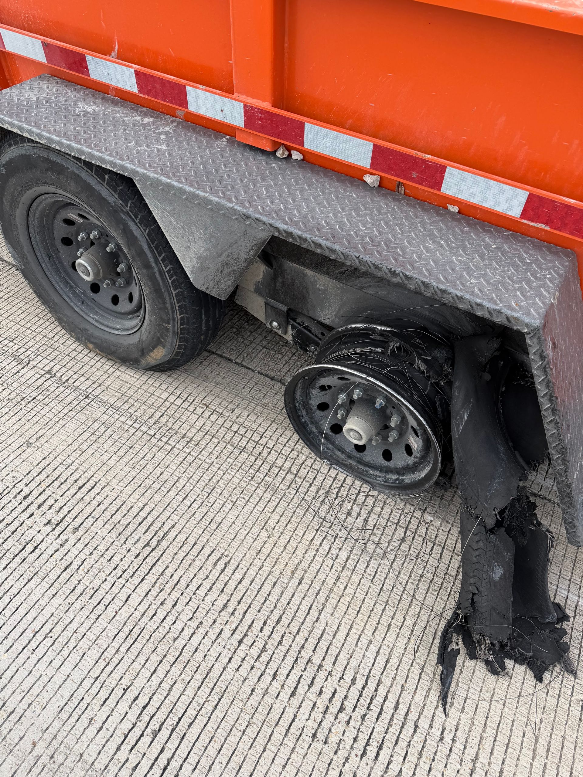 Close-up of a truck trailer’s damaged rear wheel and torn black fender on a concrete road.