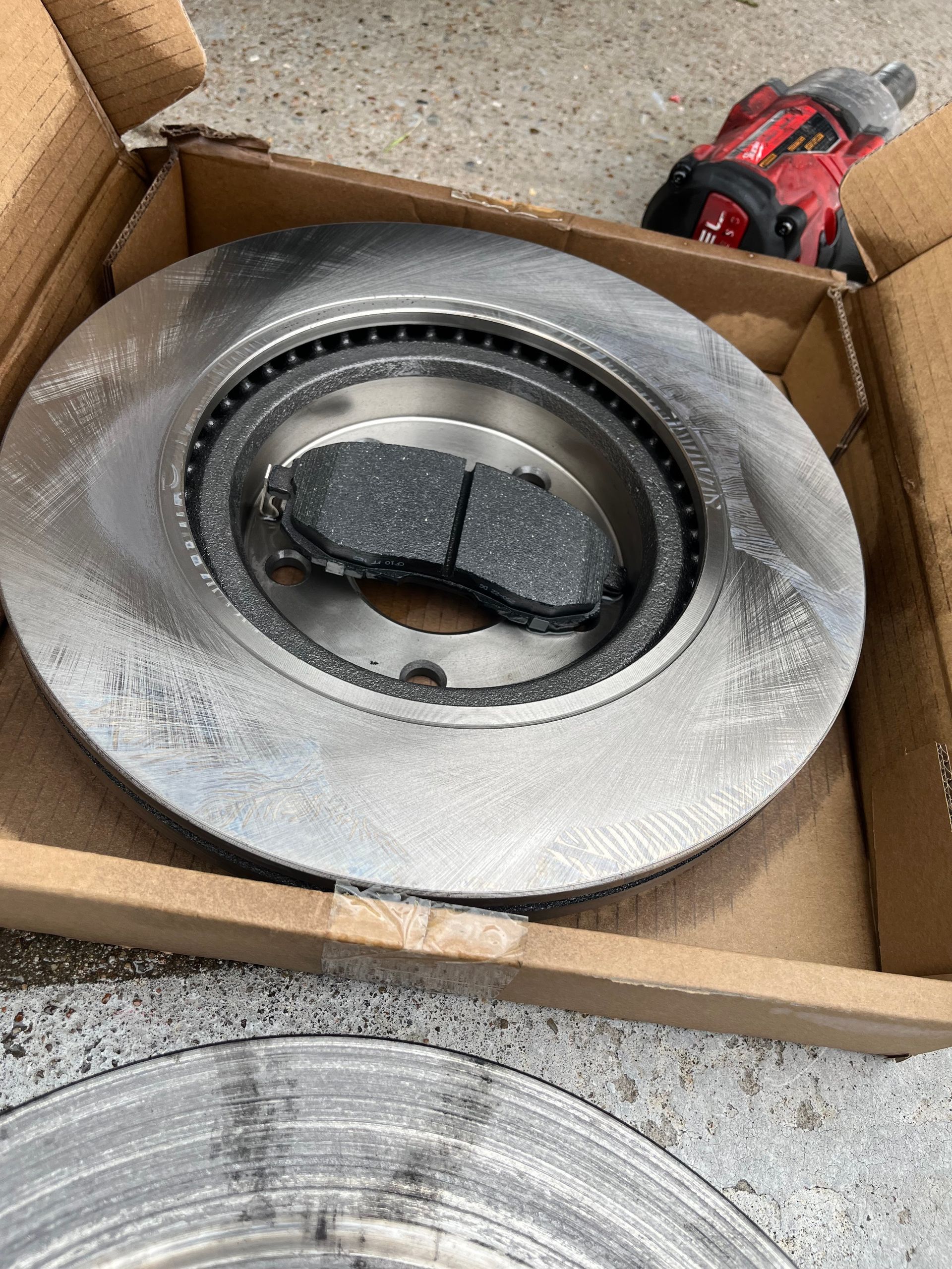 Used brake rotor and pad set in a cardboard box on a concrete floor