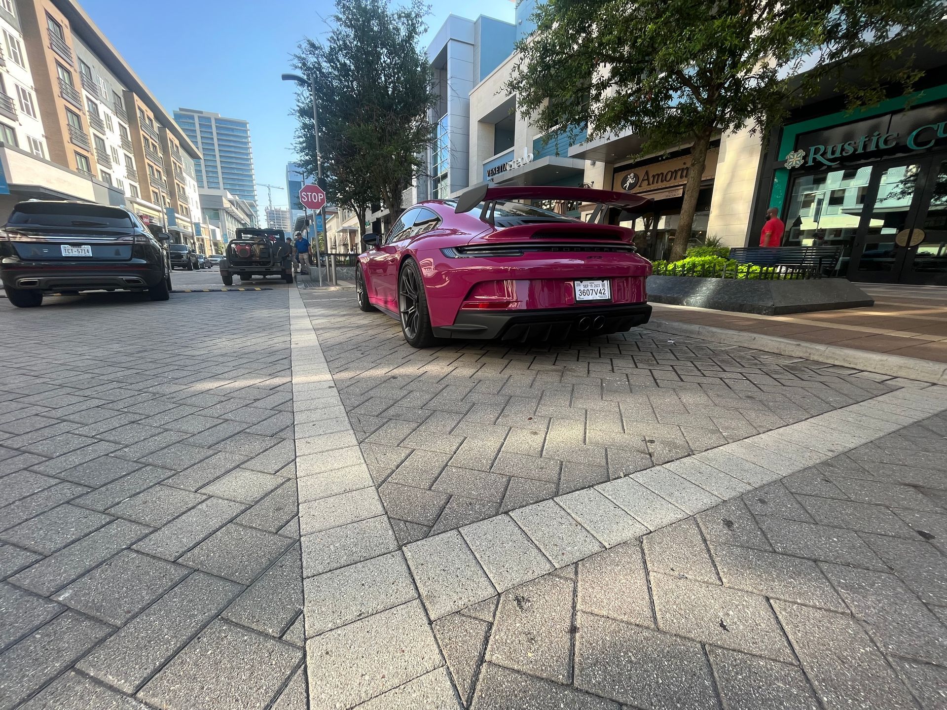 Pink sports car parked on a cobblestone city street between buildings and trees.