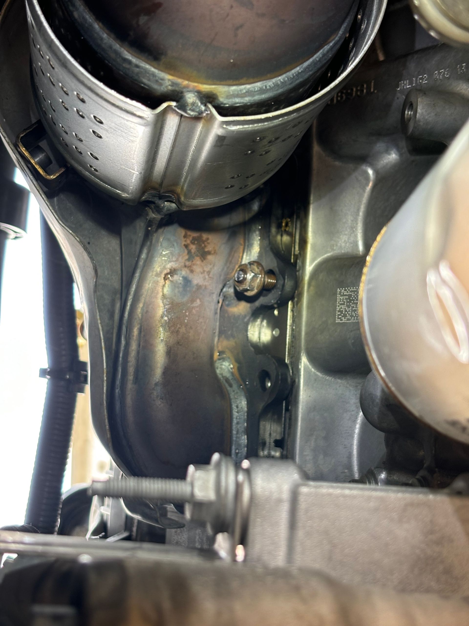 Close-up of a rusty metal engine component with bolts and a hose clamp inside a vehicle.