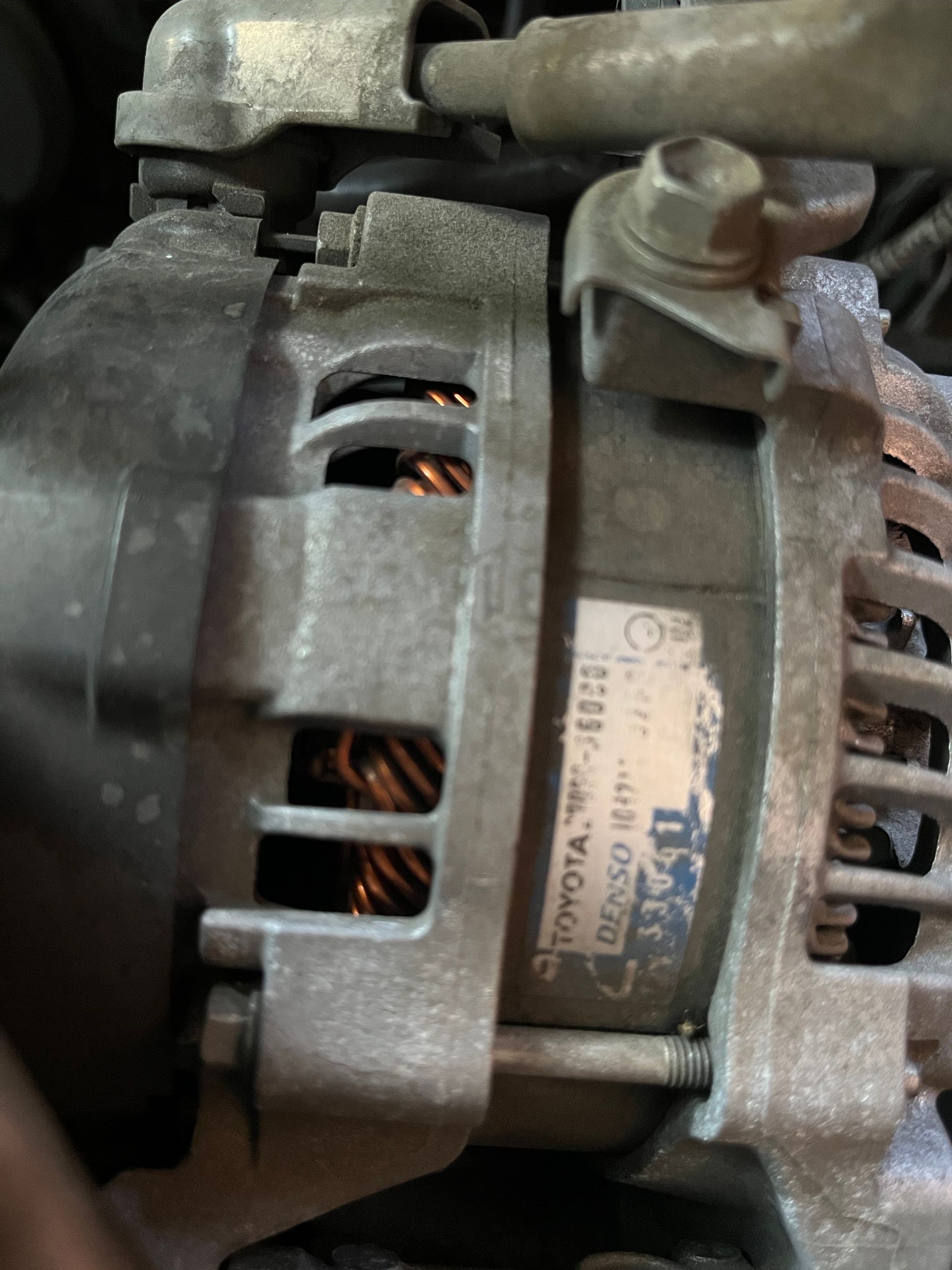 Close-up of a car alternator with visible copper coils and mounting bracket