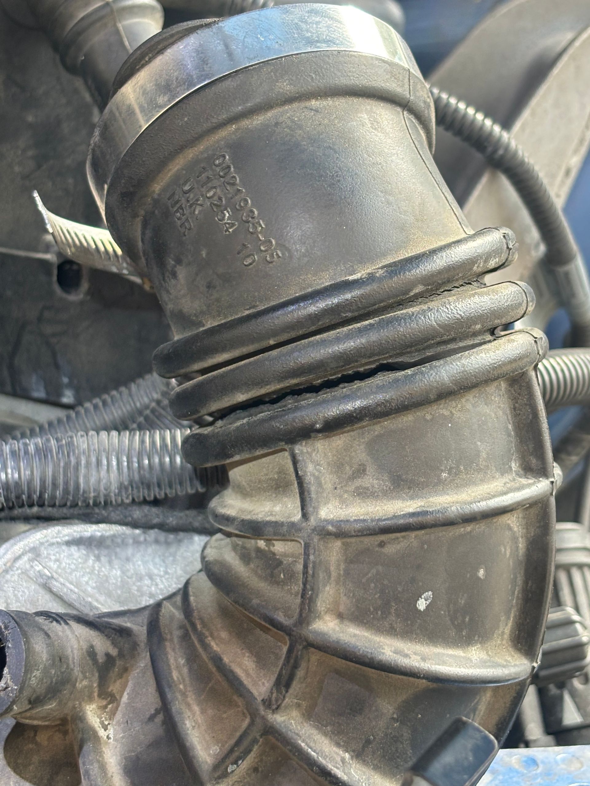 Close-up of a black rubber car intake hose with clamps and corrugated tubing.