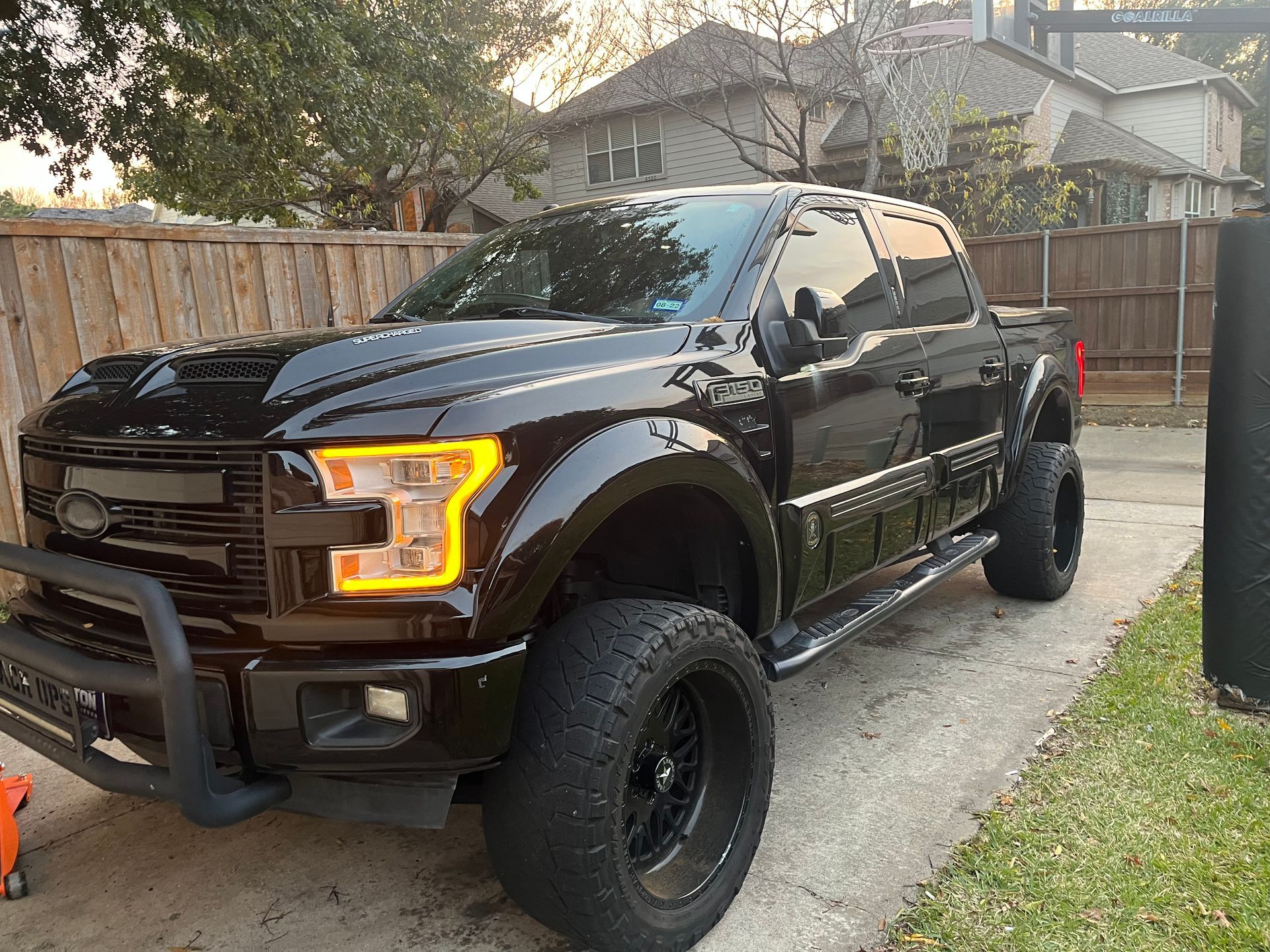 Black lifted pickup truck parked in a driveway, angled front-left view, with off-road tires and amber headlights.
