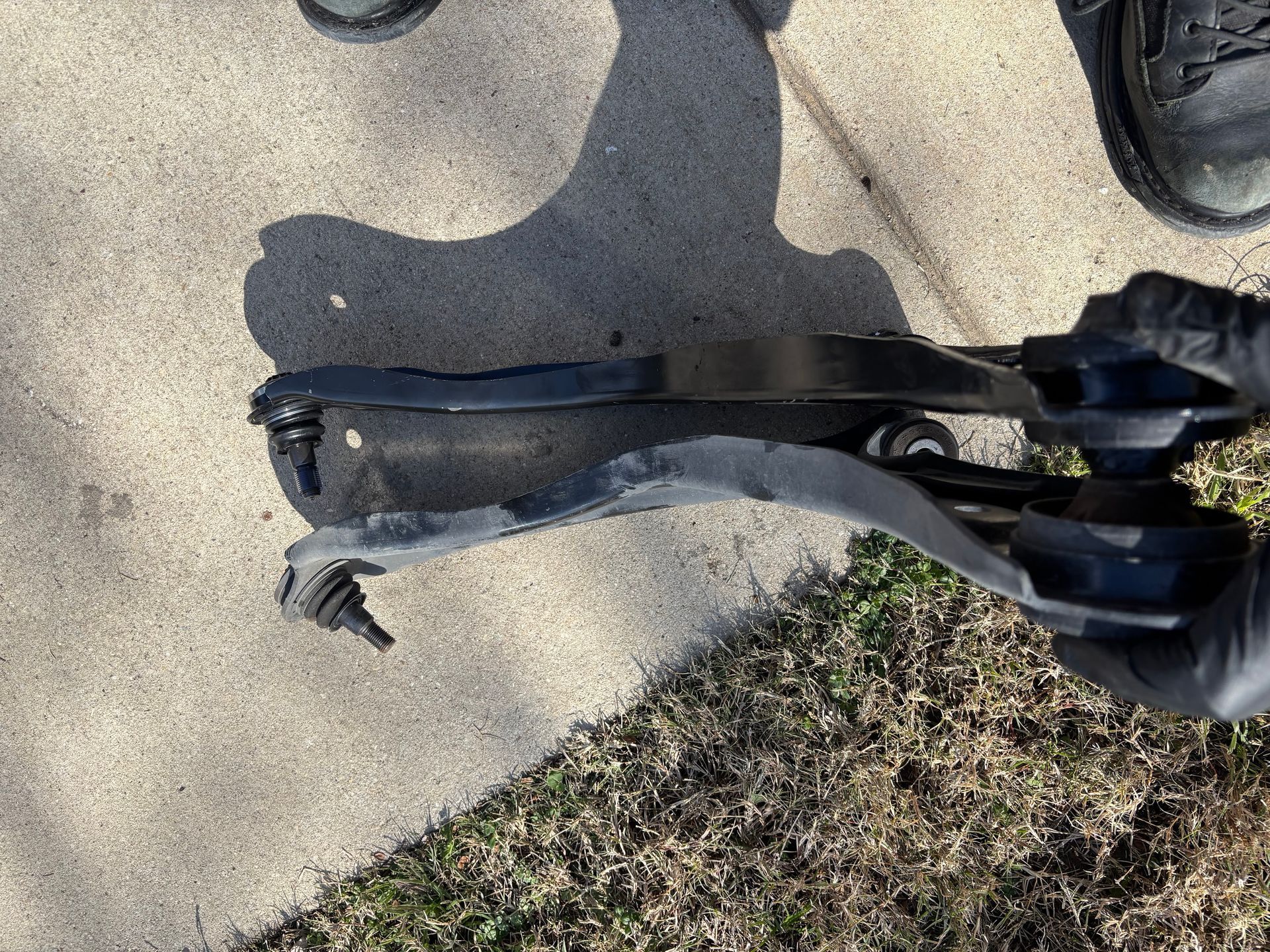 Broken black plastic tool or part lying on a sidewalk beside grass and shoes.