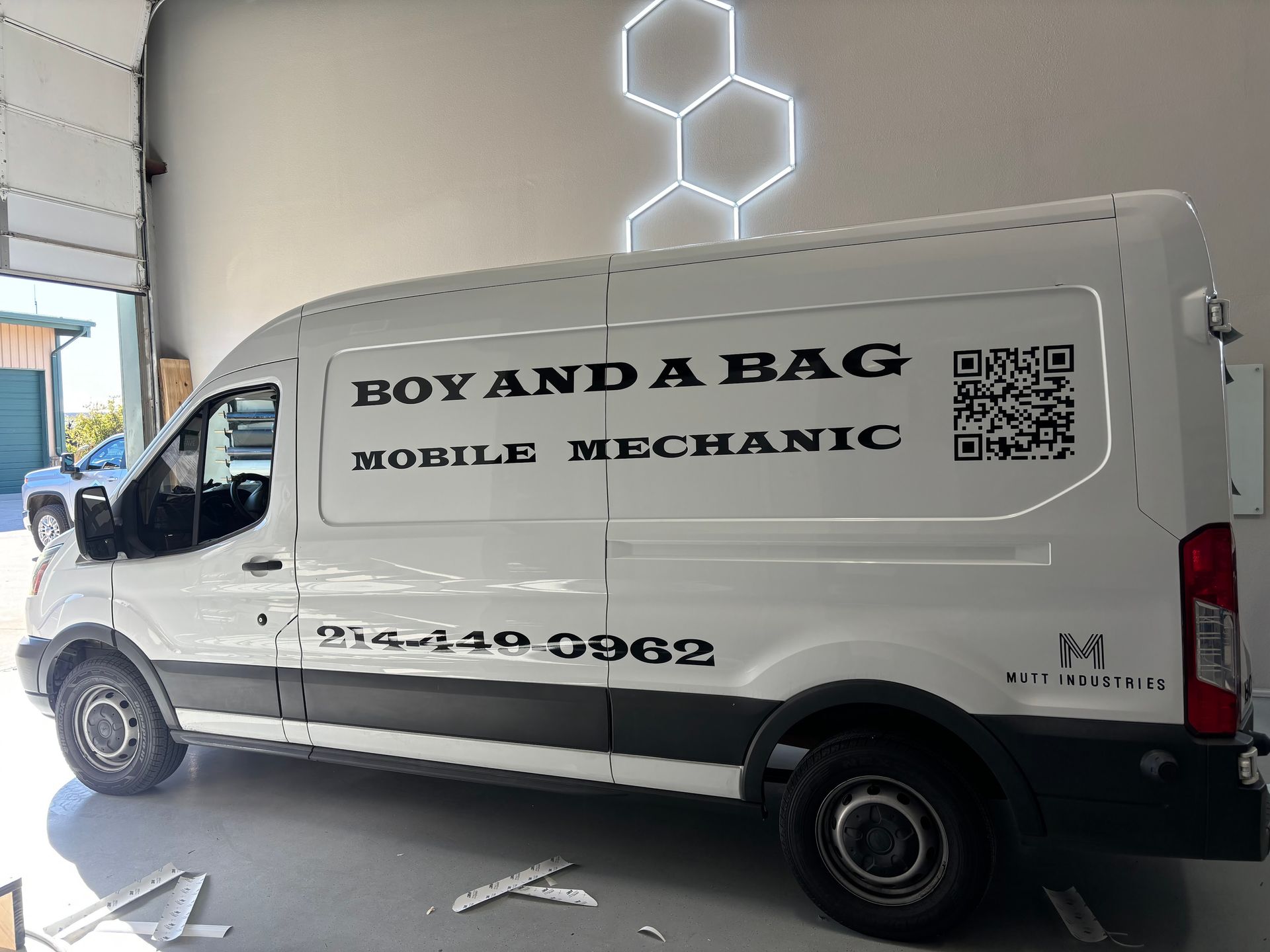 White van with “BOY AND A BAG Mobile Mechanic” signage parked indoors at a garage.