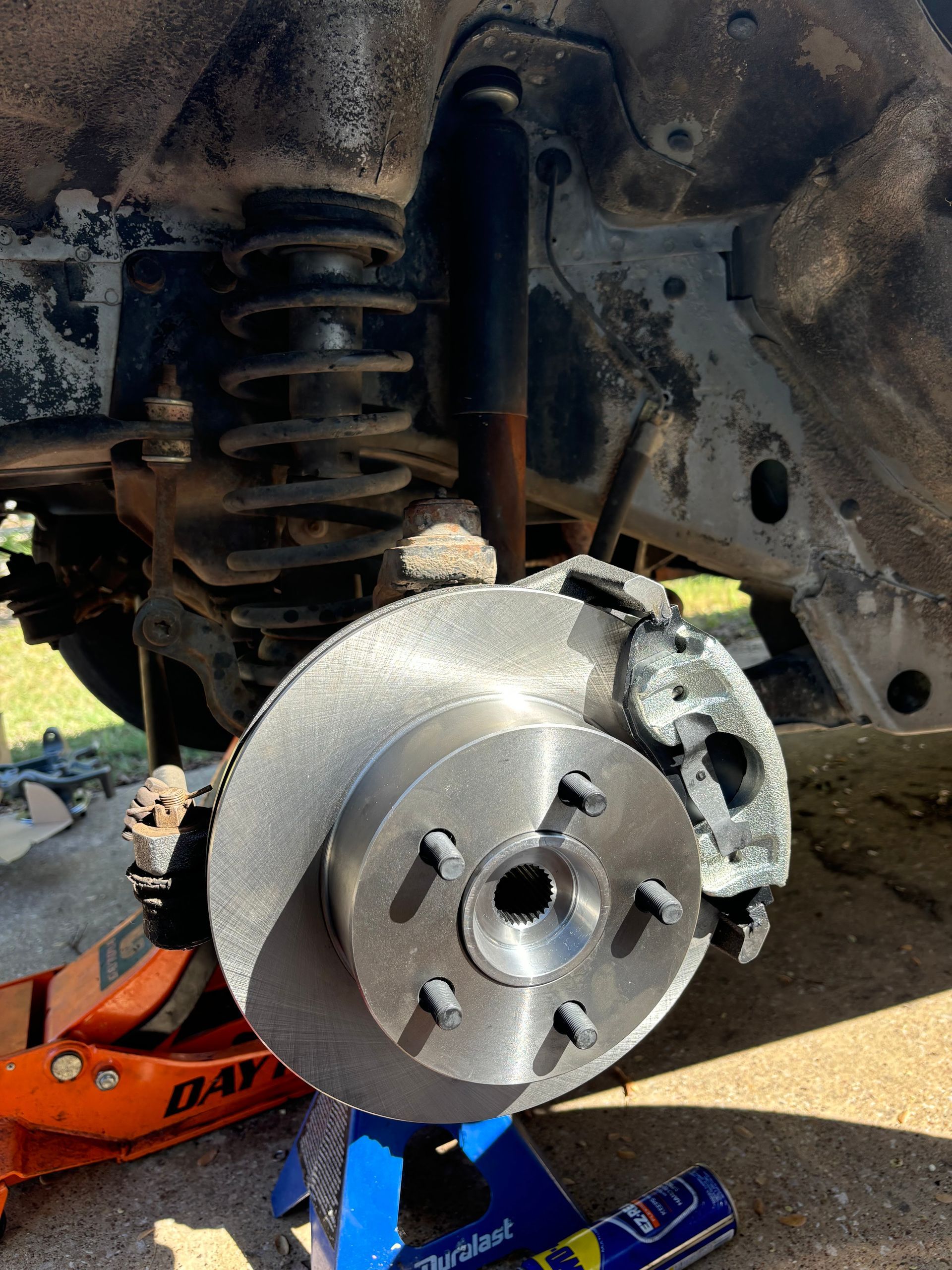 Car brake rotor and suspension exposed with wheel removed, car lifted on jack stands.
