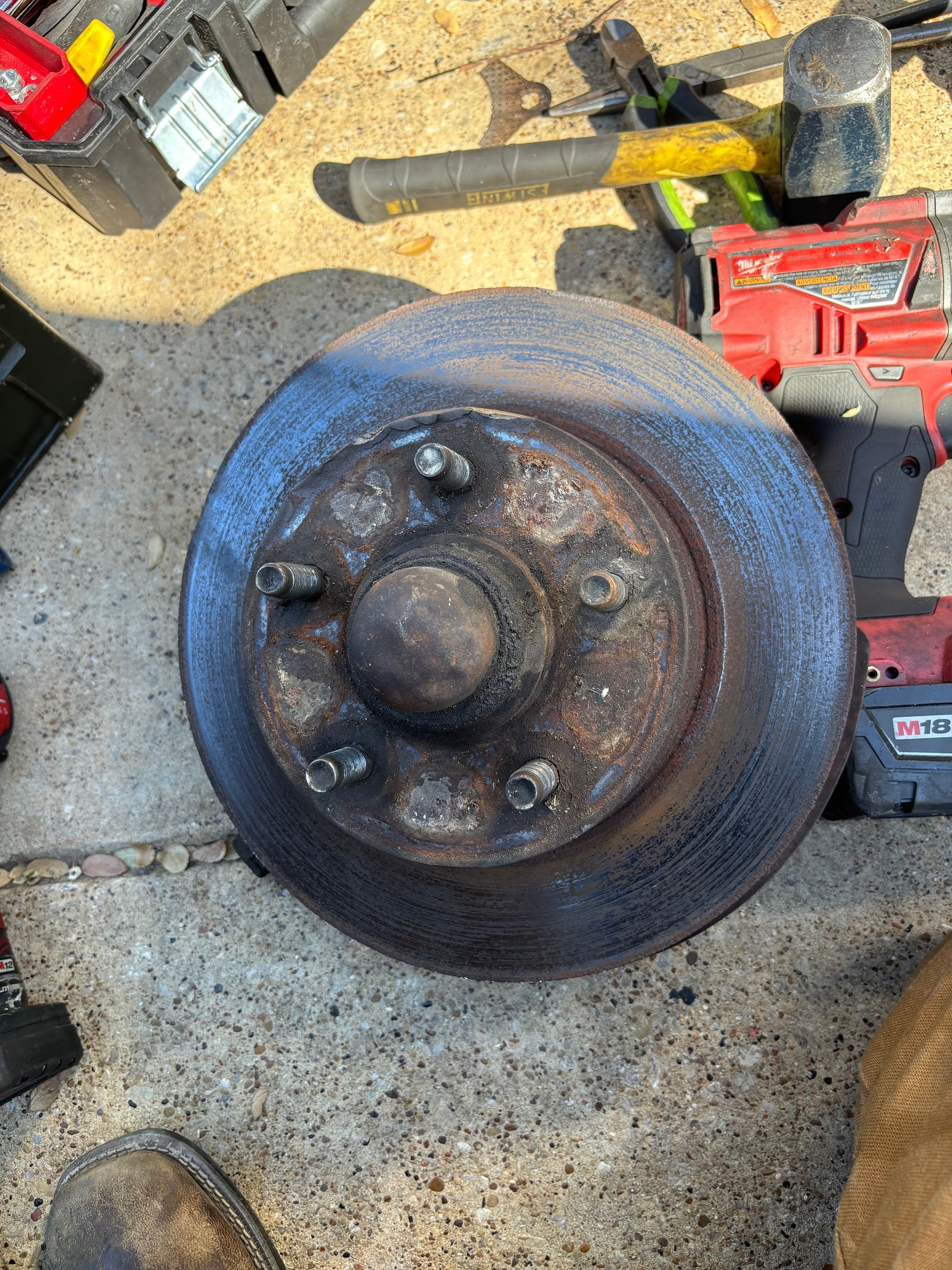 Rusty metal wheel hub on a concrete floor, surrounded by tools and equipment in a workshop.