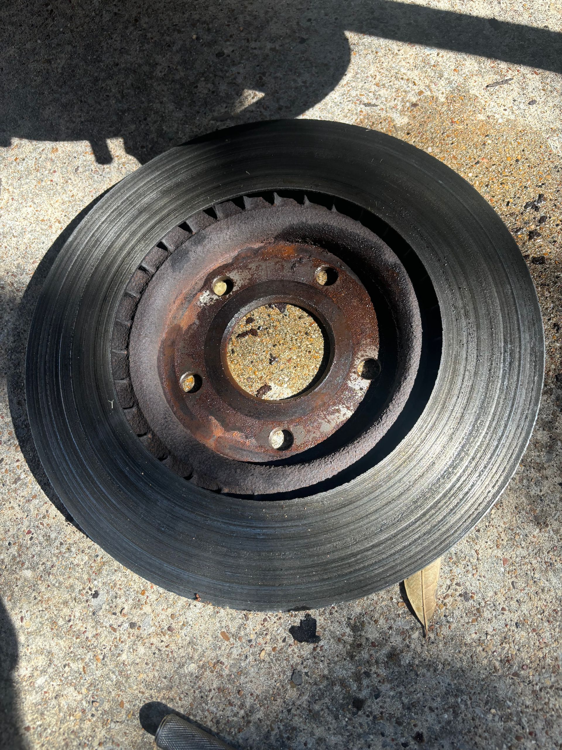 Rusty car brake disc on pavement, viewed from above.