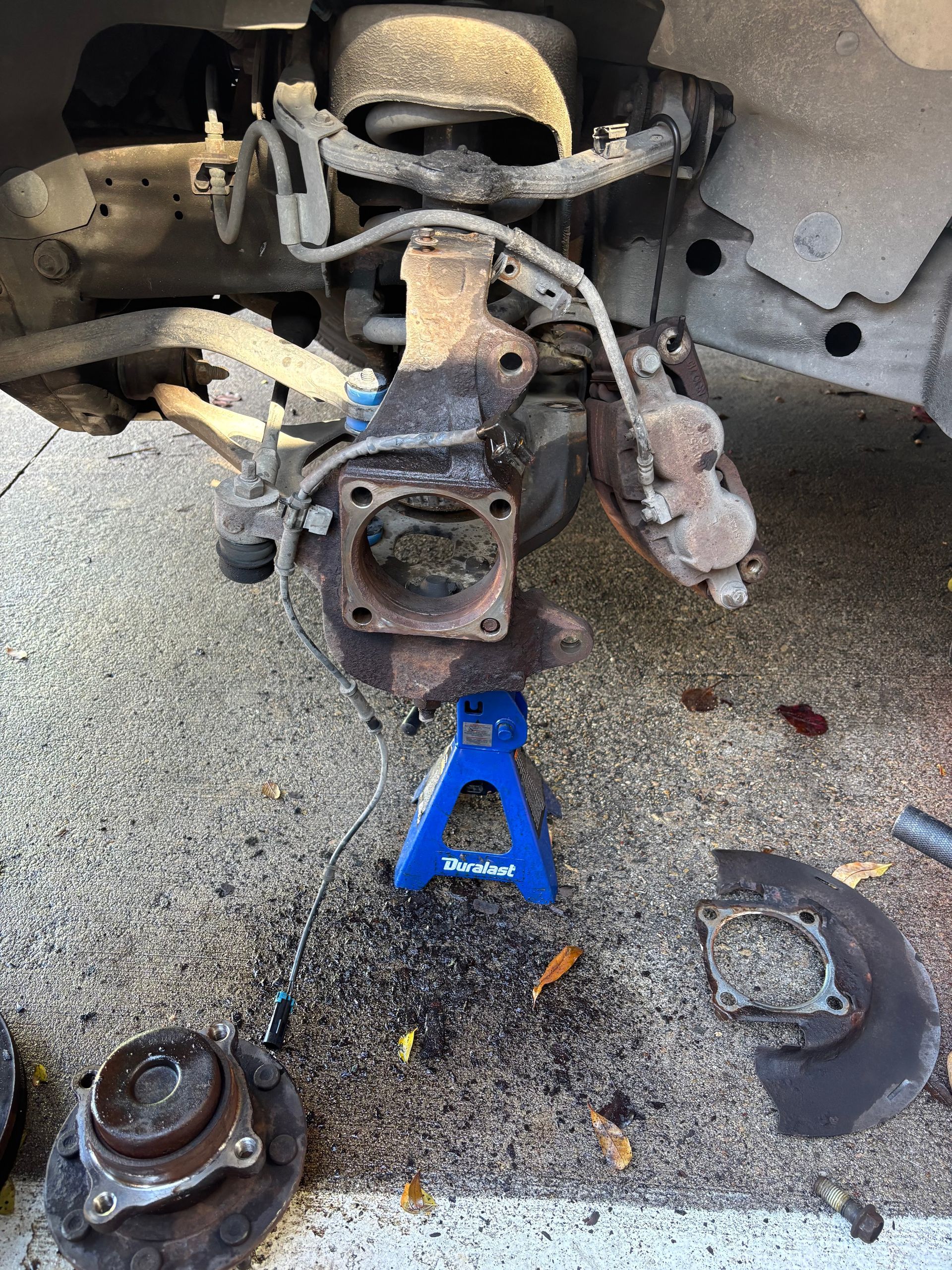 Suspension and brake parts removed from a car, with a blue jack stand under the chassis and parts on the ground.
