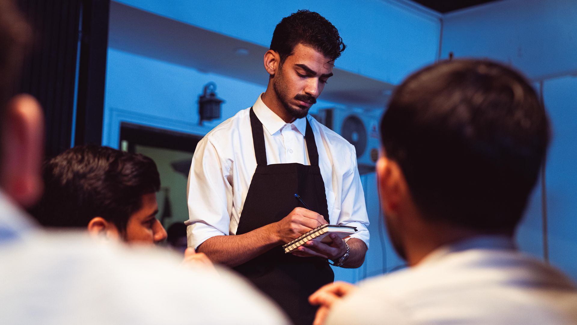 Chef preparing food in a kitchen while seated guests watch nearby