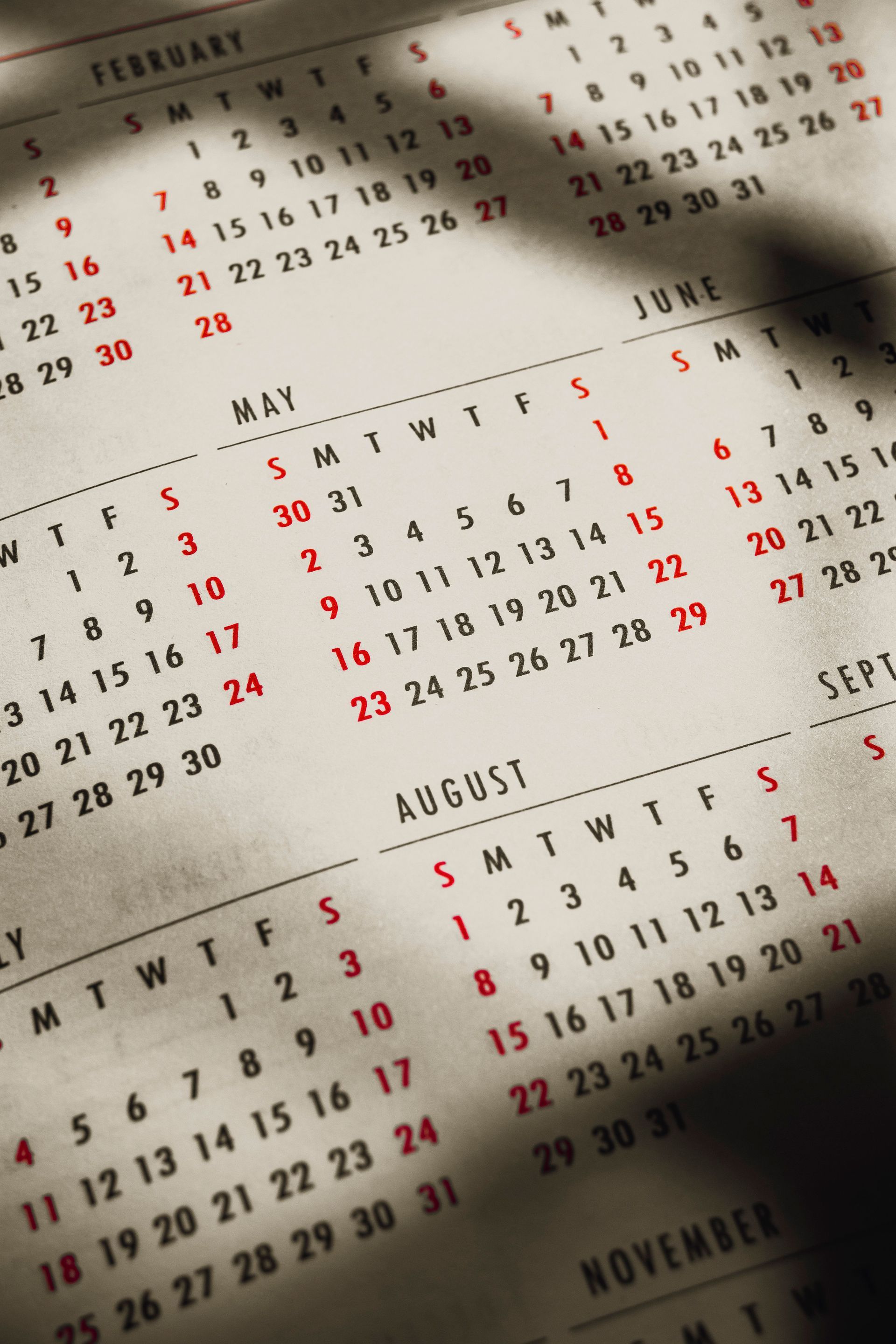 Een papieren kalender met schaduweffecten, waarop de maanden mei, juni, augustus en november zijn weergegeven met rode zondagen.