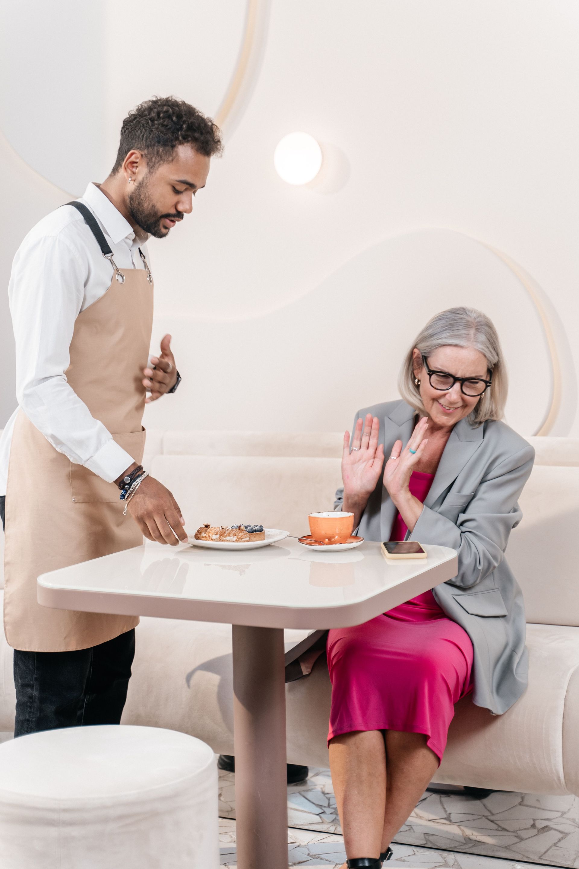 Man serving dessert to a smiling seated woman in a bright living room