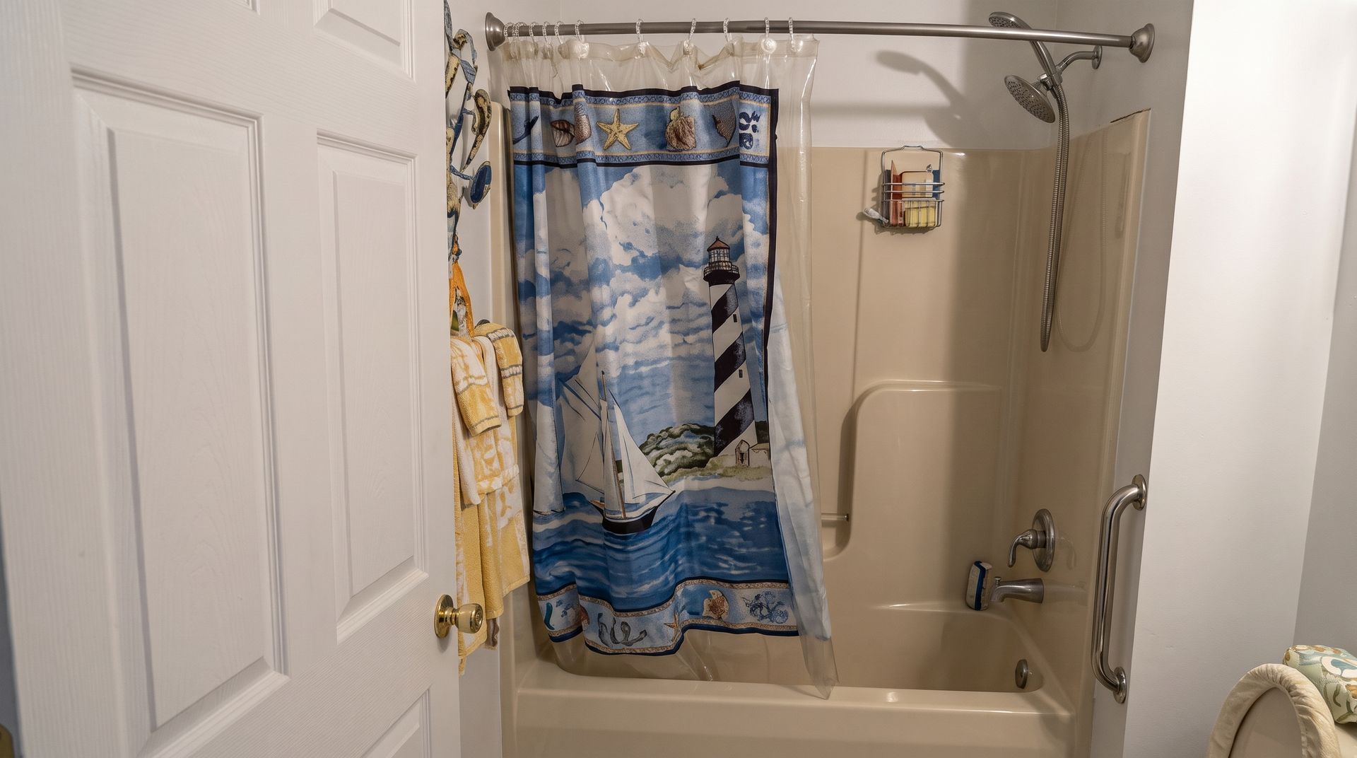Small bathroom with beige tub, shower curtain, and blue patterned towels hanging inside.