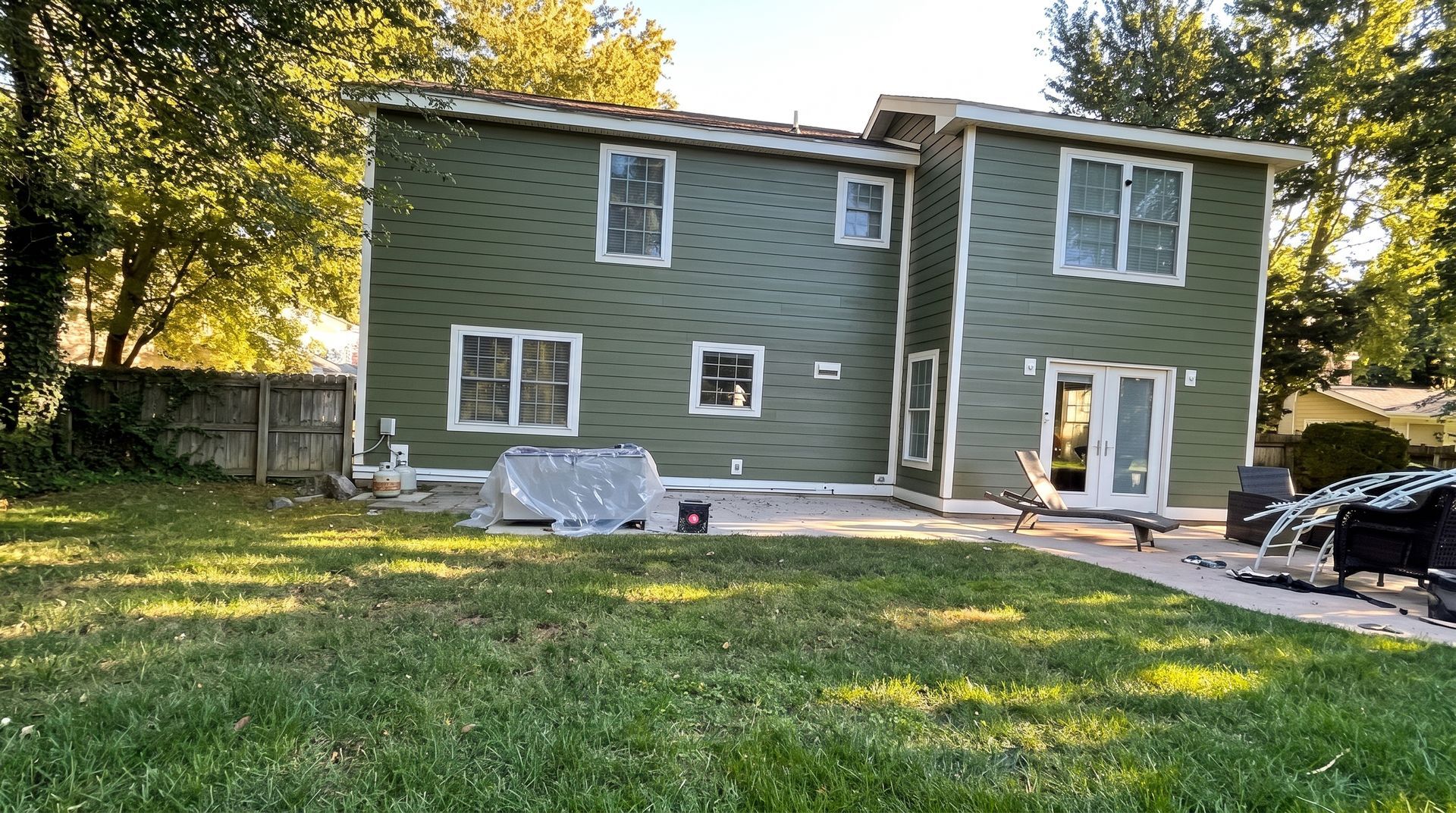 Green two-story house with white trim and large windows, viewed from a grassy backyard.