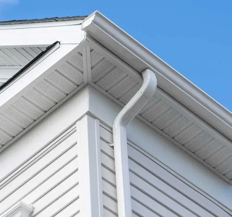 White house corner with gutter and downspout against a blue sky