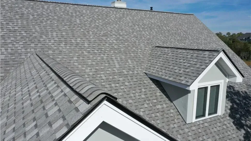 Gray shingled roof with two dormer windows under a clear blue sky