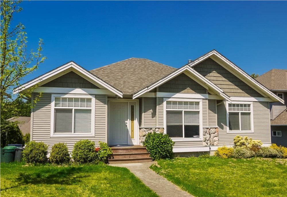 Single-story suburban house with gray siding, white trim, a front lawn, and a bright blue sky