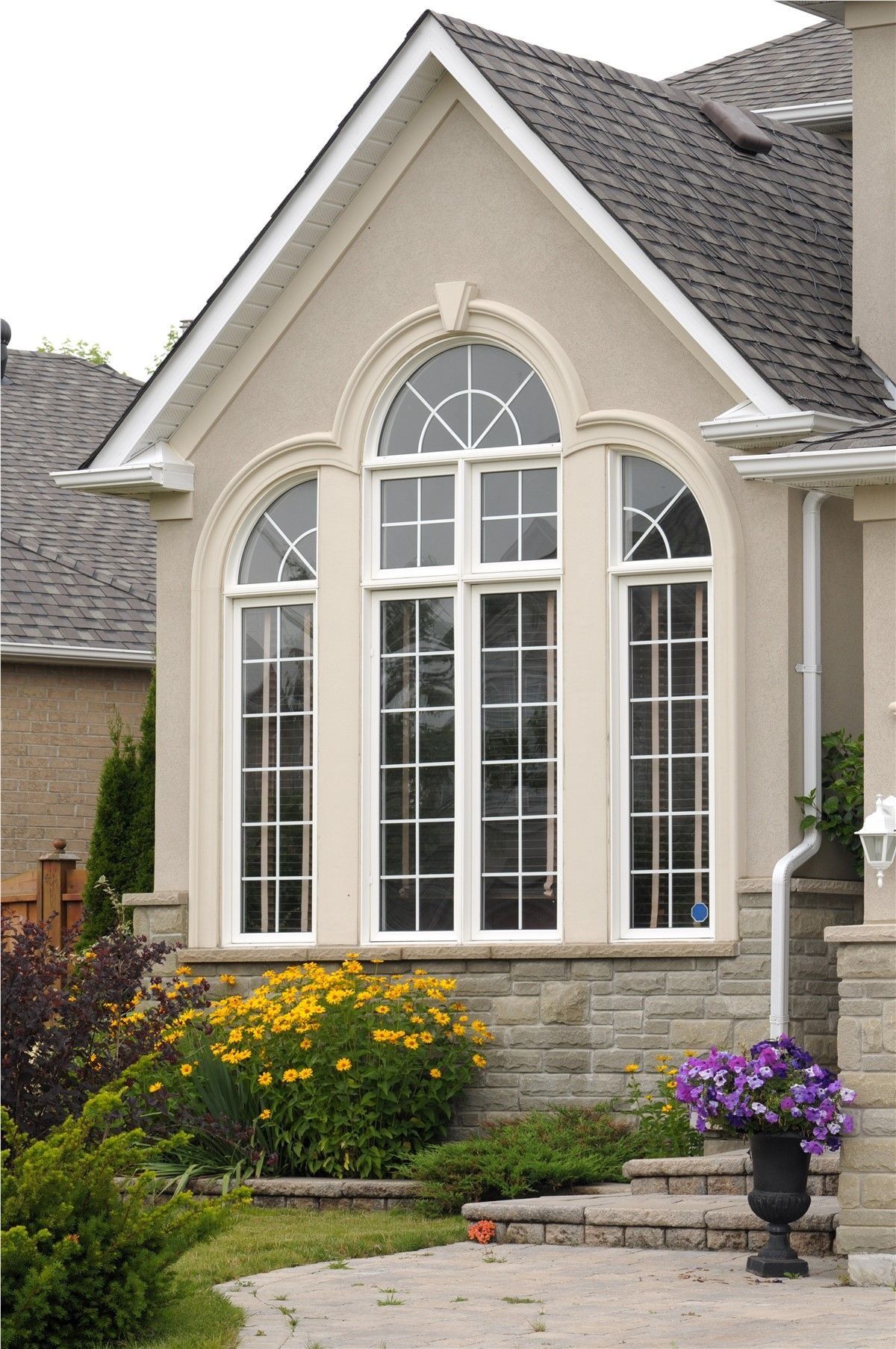 Tall arched front windows on a beige brick house with flower beds and stone steps