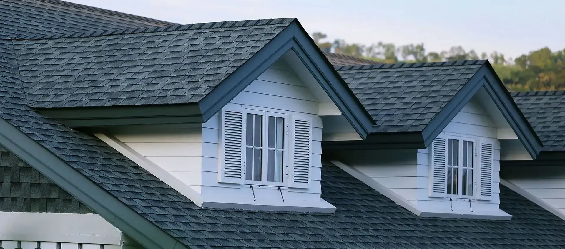Gray shingled house roof with two dormer windows and white trim