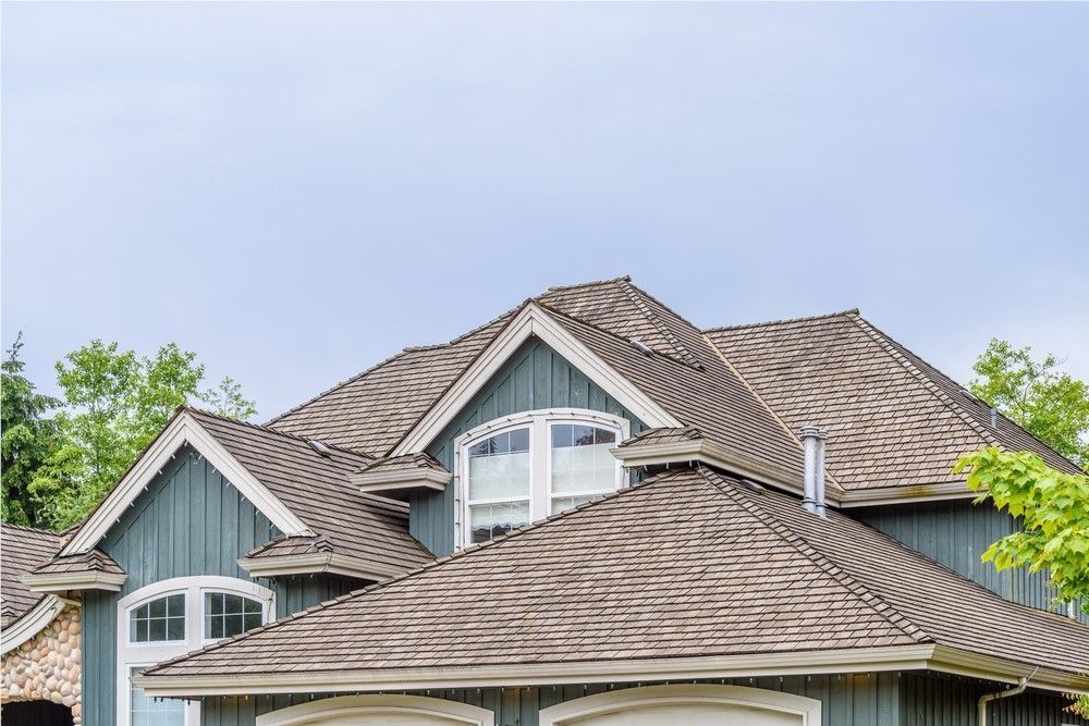 Large suburban house with gray shingled roof and dormer windows under a blue sky