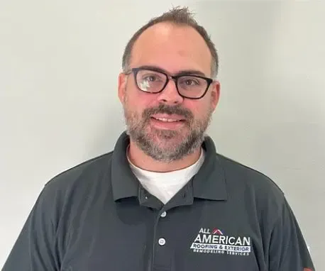 Smiling man in glasses wearing a dark gray American Services polo against a plain light wall