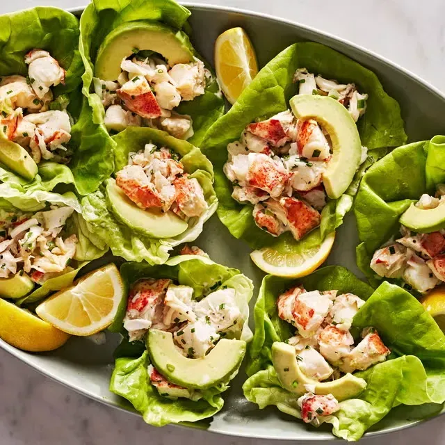 a plate of food with chicken , avocado , tomatoes and limes on a table .
