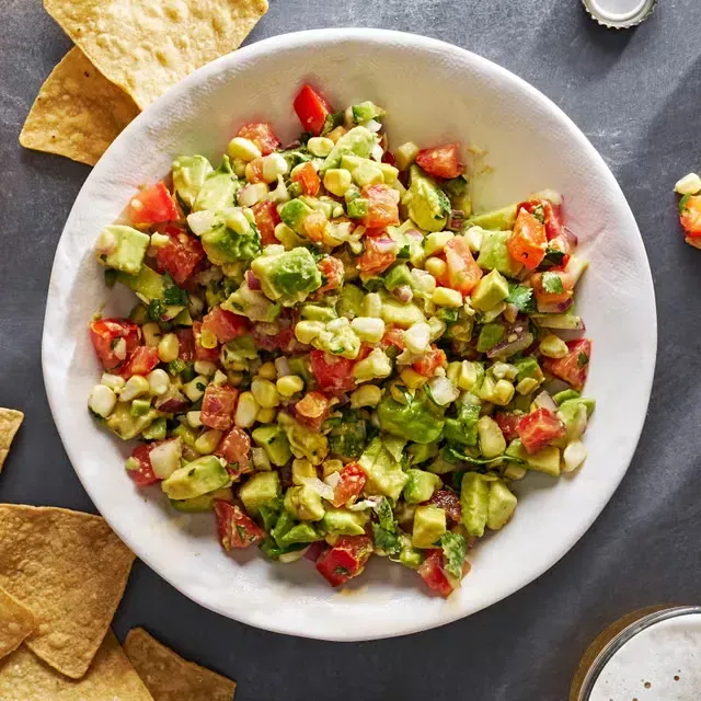 a plate of food with chicken , avocado , tomatoes and limes on a table .