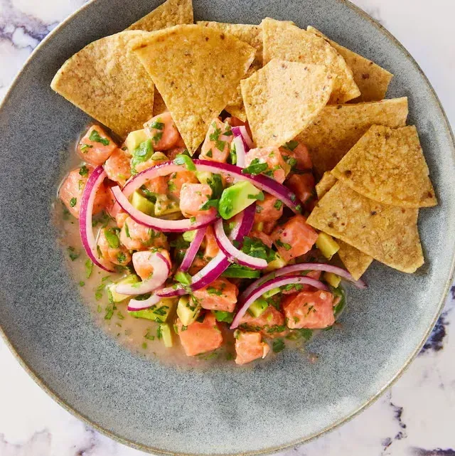 a plate of food with chicken , avocado , tomatoes and limes on a table .