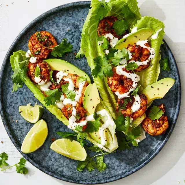 a plate of food with chicken , avocado , tomatoes and limes on a table .