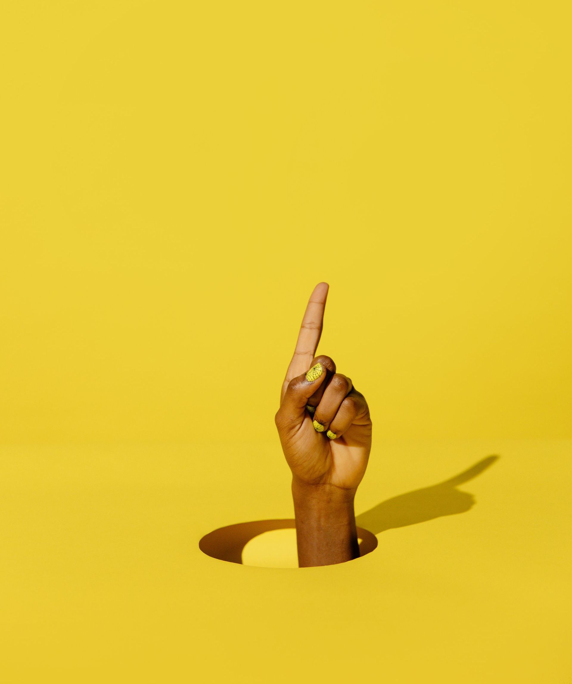 Hand with raised index finger emerging from a yellow surface with a shadow