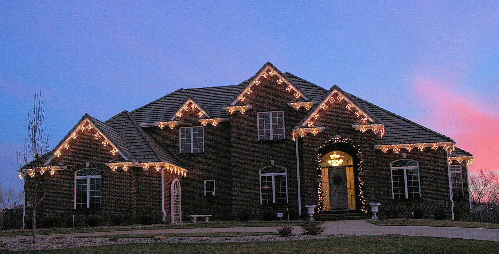 Stone house at dusk with warm roofline lights and a pink-blue sky.