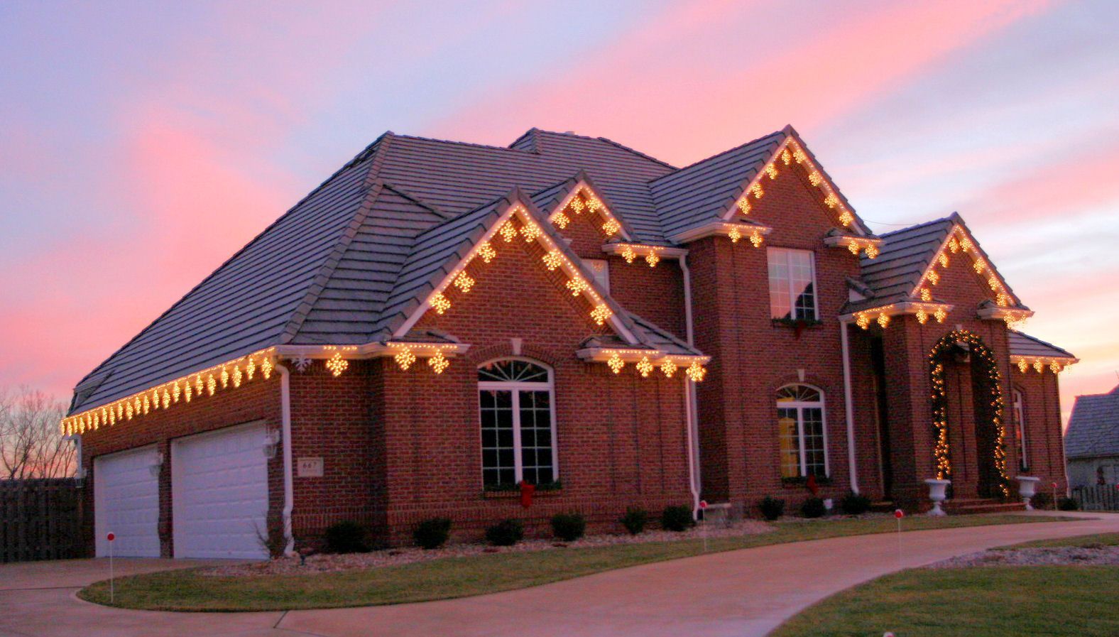 Brick house with festive string lights at dusk under a pink sunset sky