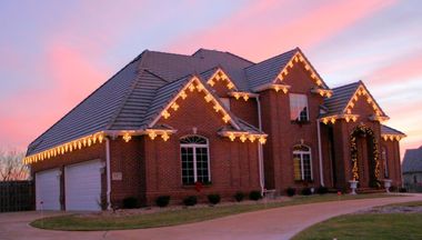 Brick house with festive string lights at dusk under a pink sunset sky