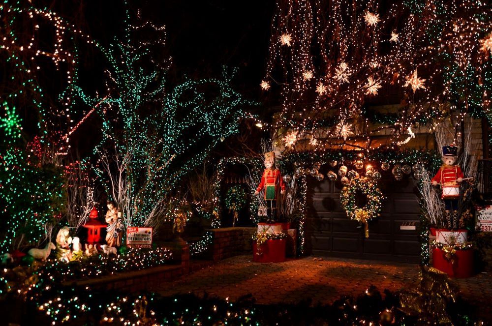 Holiday light display with illuminated trees, toy soldiers, and a decorated house at night