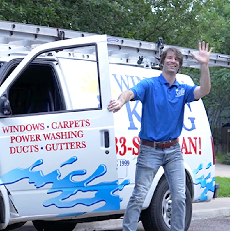 Man in blue shirt waving beside a white cleaning service van with red and blue lettering.