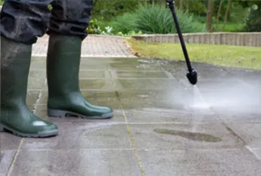 Person in green boots pressure-washing a wet sidewalk outdoors