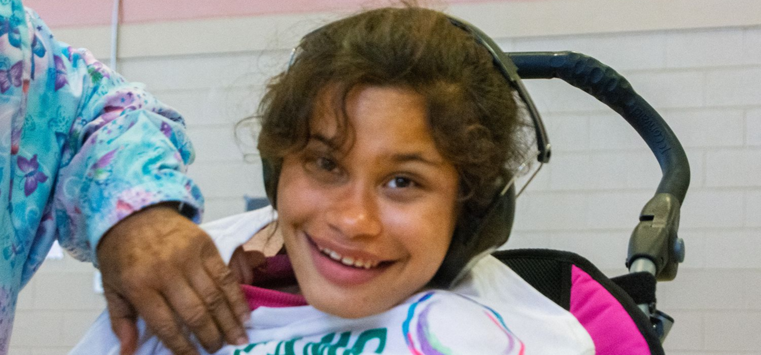 A female student of Orange Grove School smiles while seated in her stroller.