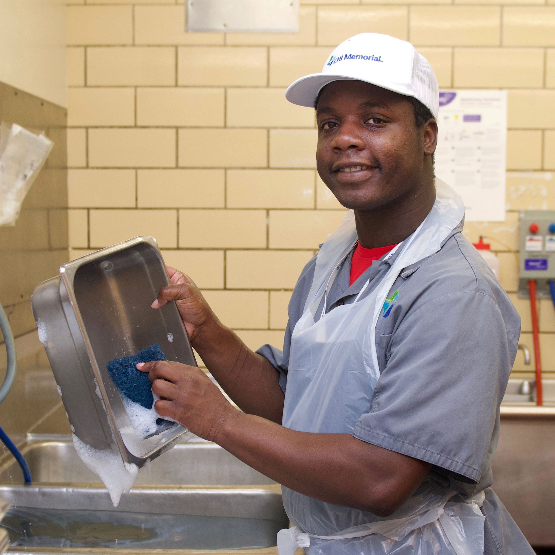 A man in an apron washes dishes in a kitchen as part of Orange Grove's Employment Services.
