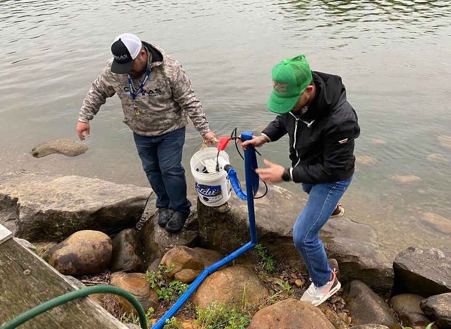 Two male Fishing Tournament participants haul a bucket of caught fish out of the Tennessee River.