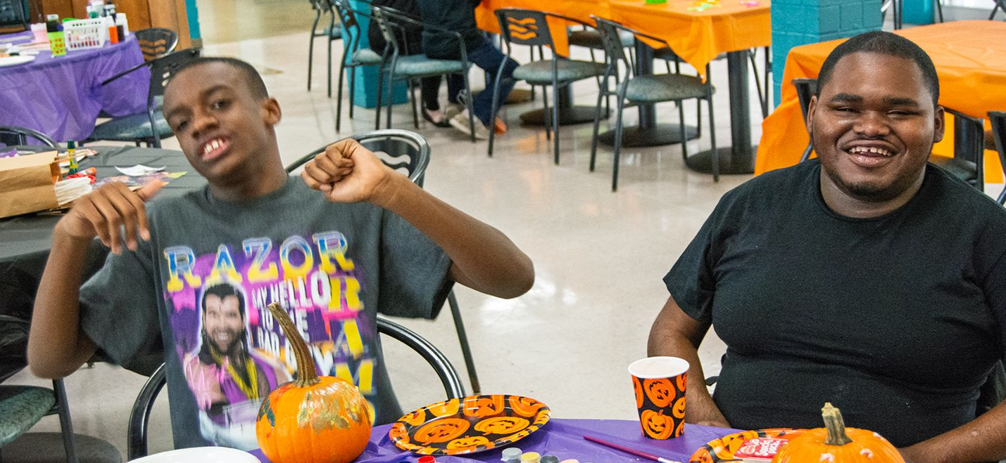 Two male Orange Grove School students decorating pumpkins during a Halloween party.