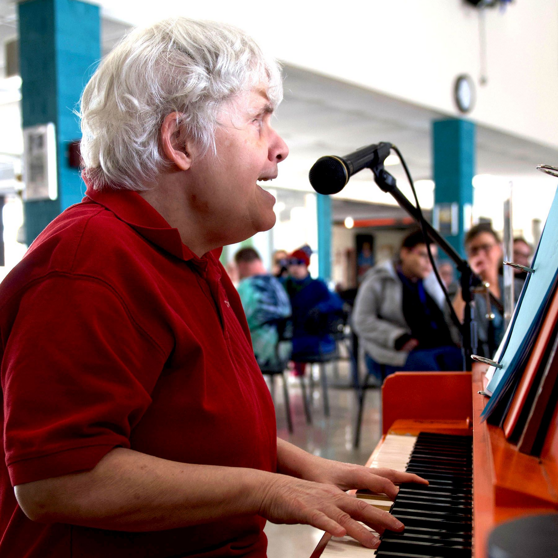 A woman singing into a microphone while playing piano during an Orange Grove choral performance.